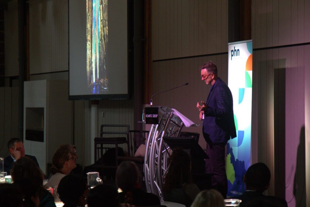 A portrait of Paul Pritchard on the stage of the Primary Care Conference